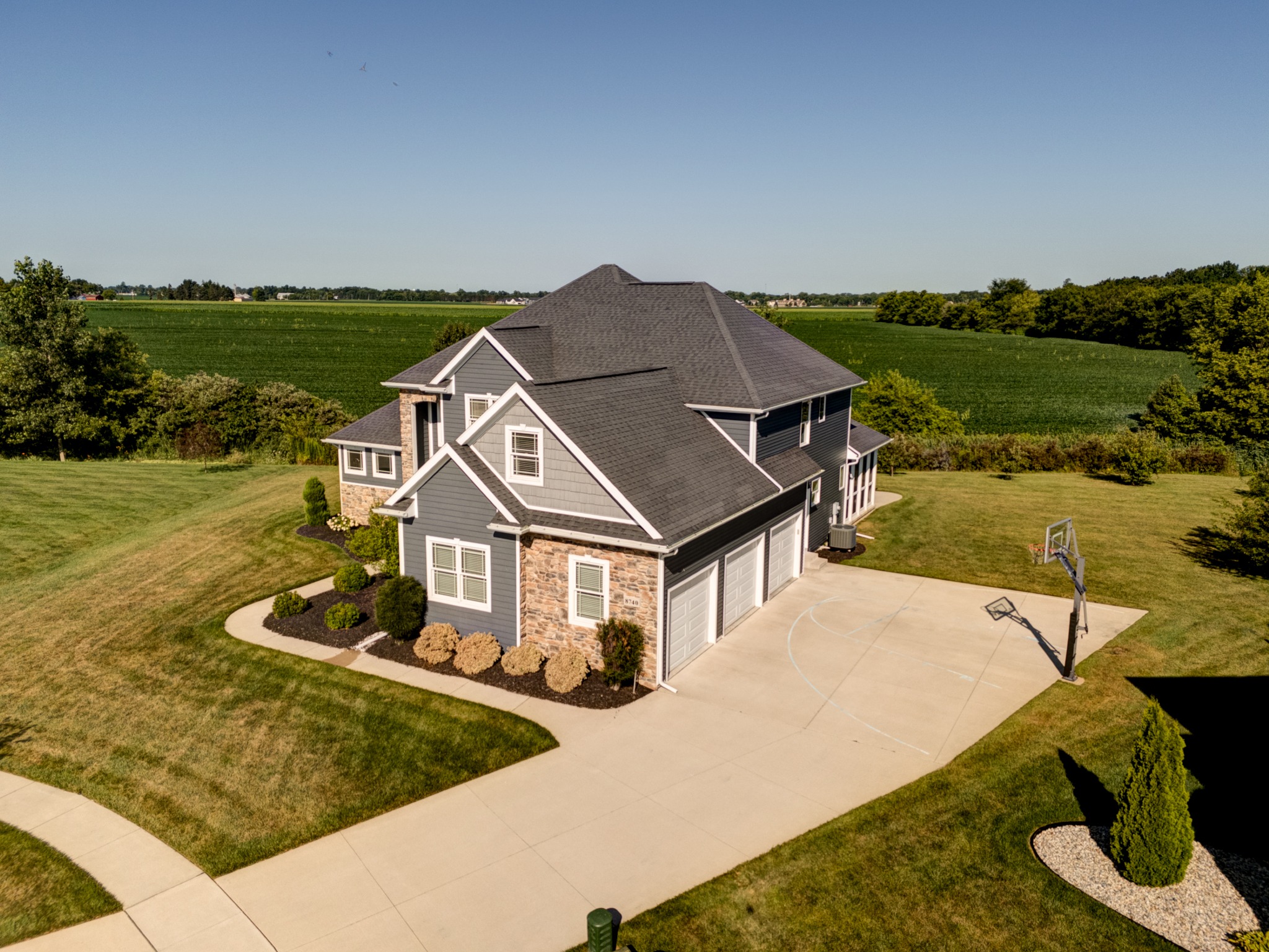 Aerial view of the home, three-car garage, driveway and open fields