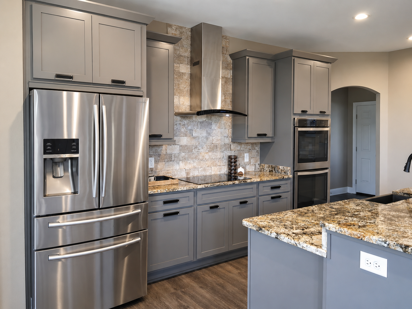Stainless refrigerator, range hood, cabinetry and stone backsplash